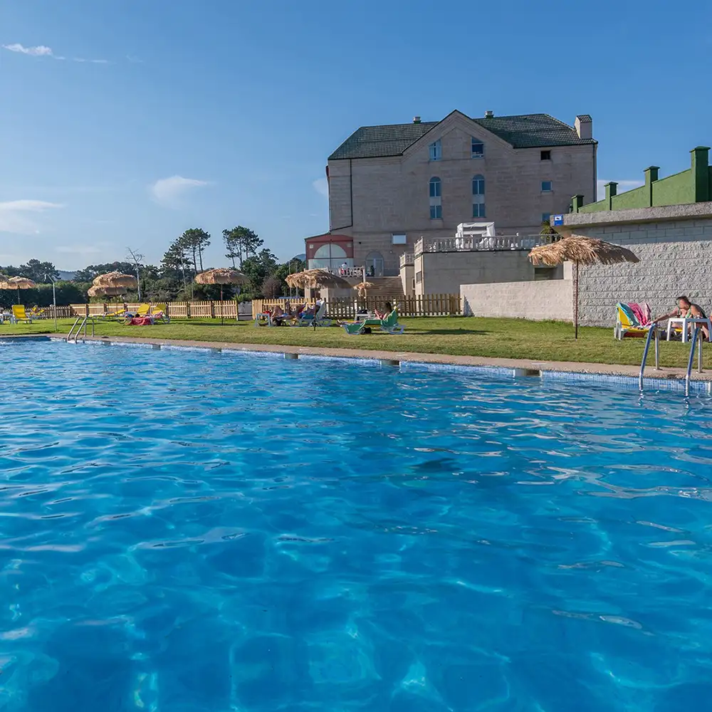 Piscina al aire libre con sombrillas y edificio al fondo bajo cielo azul
