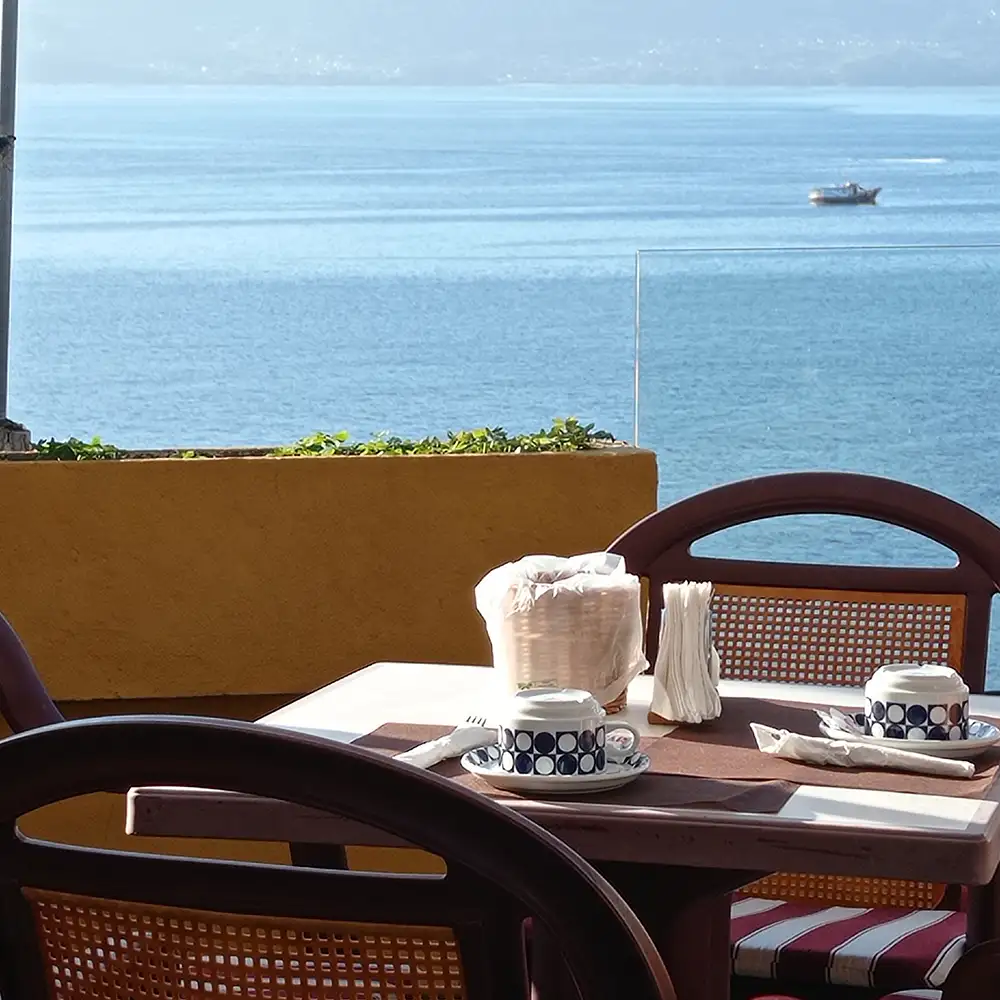 Mesa con vasos y embalajes junto al mar, lancha al fondo.