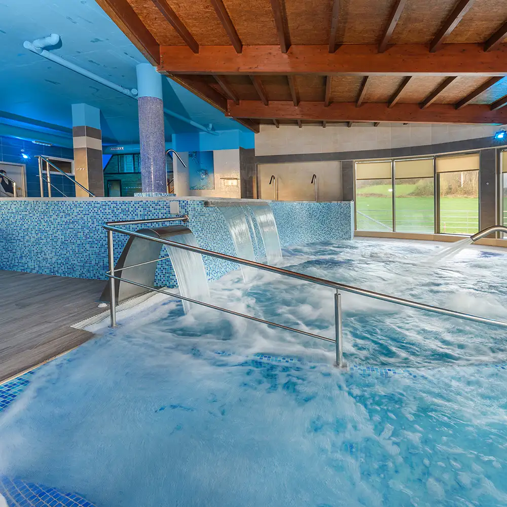Piscina cubierta con chorros de agua y techo de madera, vista interior
