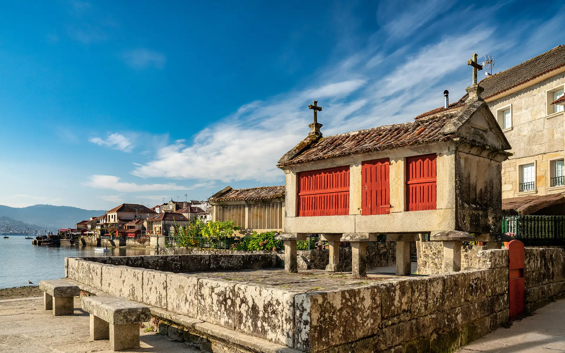Casas de piedra con techos de teja y puertas rojas junto al r&iacute;o, cielo azul