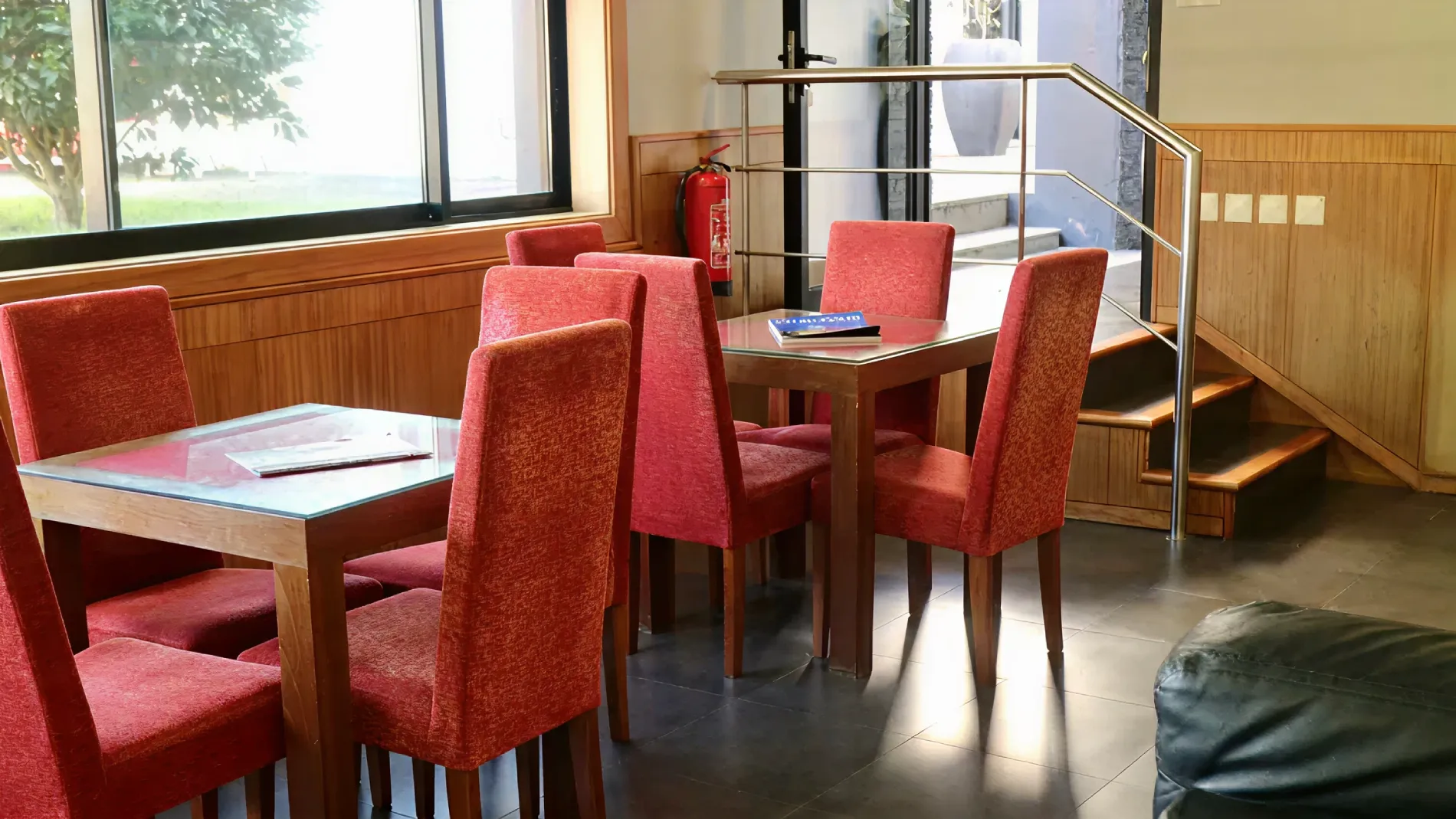 Sala de jantar com mesas e cadeiras vermelhas, ao lado de um vidro e extintor