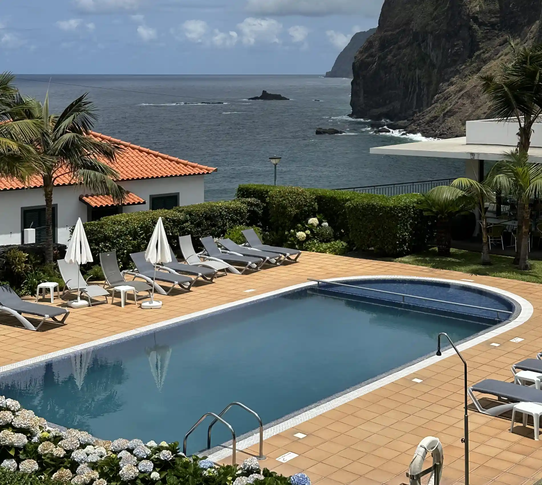 Piscina e cadeiras ao sol com vista do oceano e fal&eacute;sias rochosas ao fundo