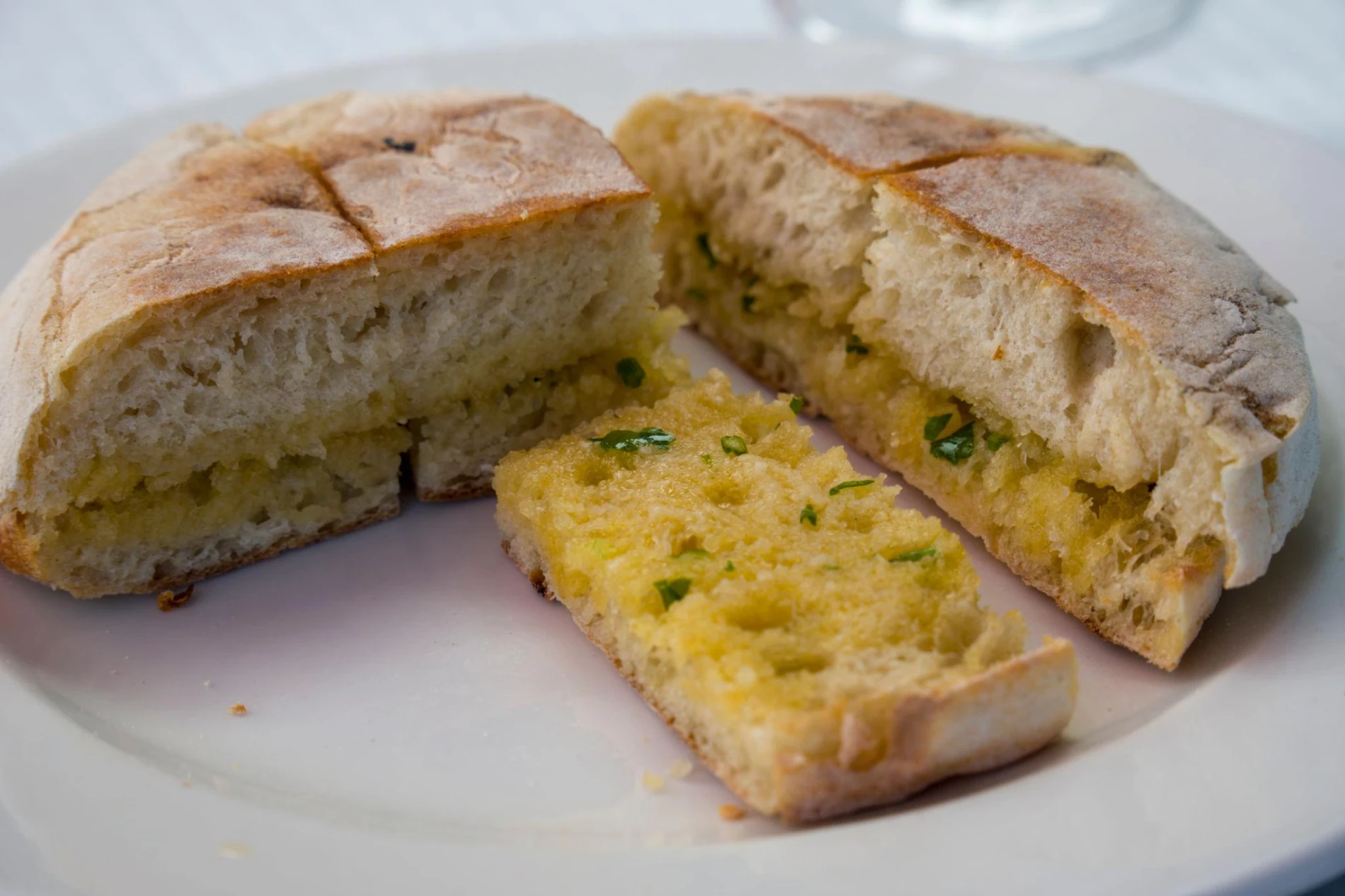 P&atilde;o caseiro fatiado com recheio de queijo e ervas, servido em prato branco