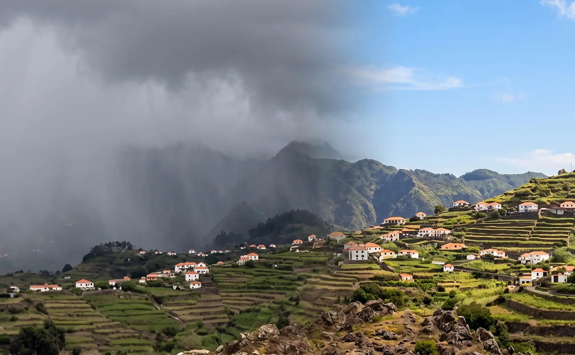 Vale verde com casas e montanhas, com nevoeiro sobre as encostas