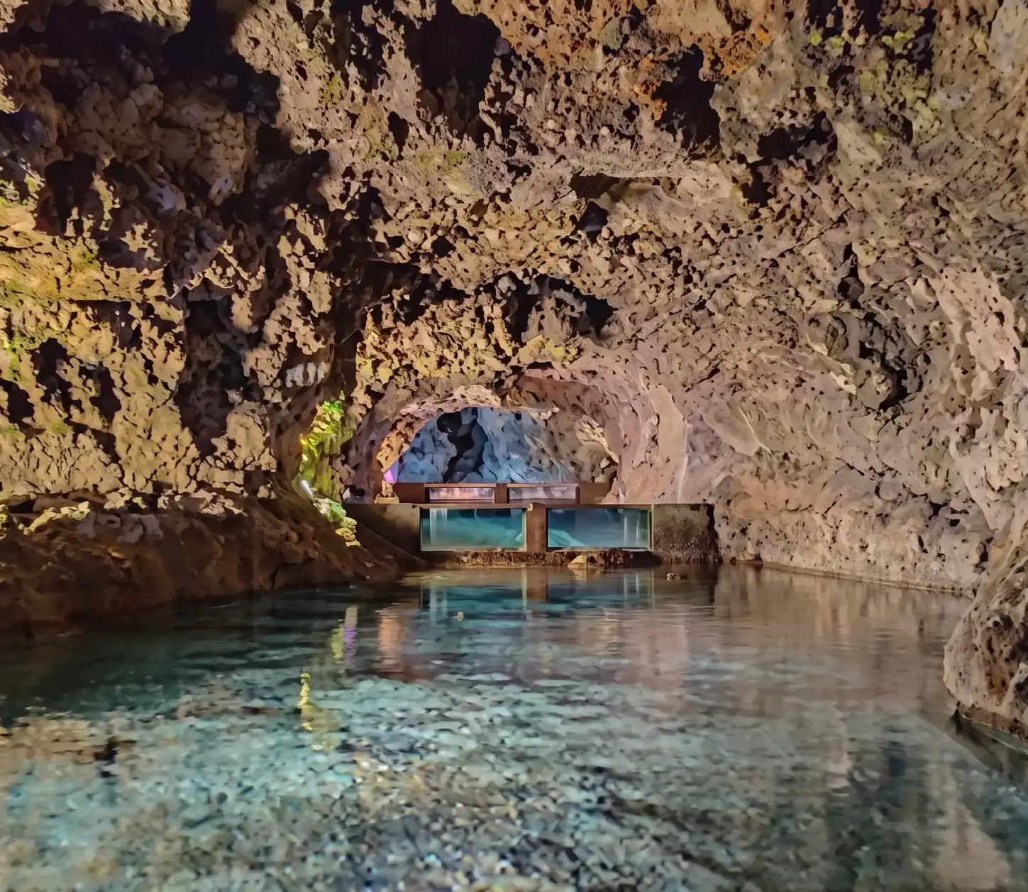 Caverna com lago e passarela iluminada, reflexo na &aacute;gua.