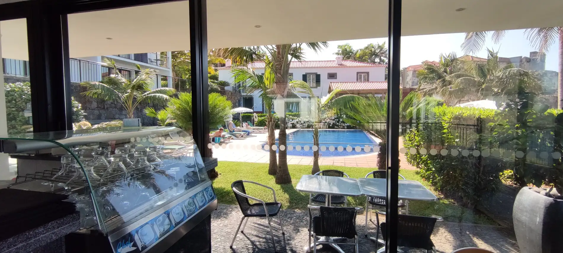 Vista de churrasqueira e piscina em jardim com palmeiras e cadeiras ao ar livre