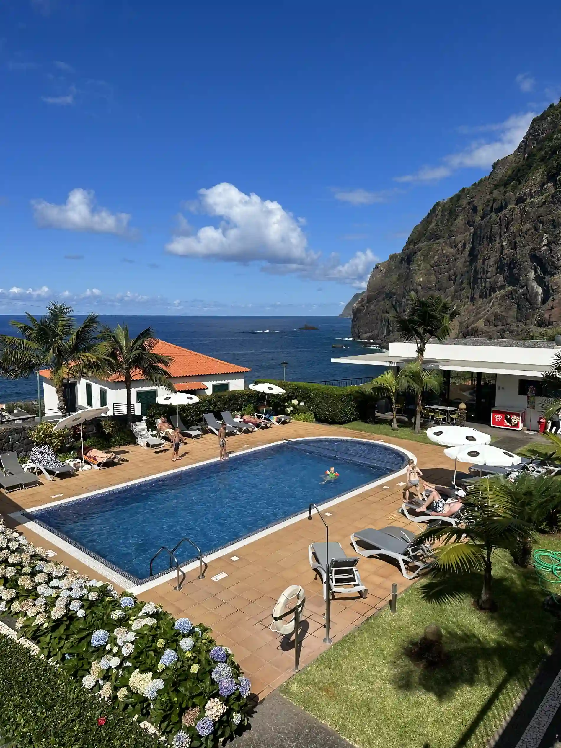 Piscina e jardim de hotel com vista para o mar e montanha ao fundo
