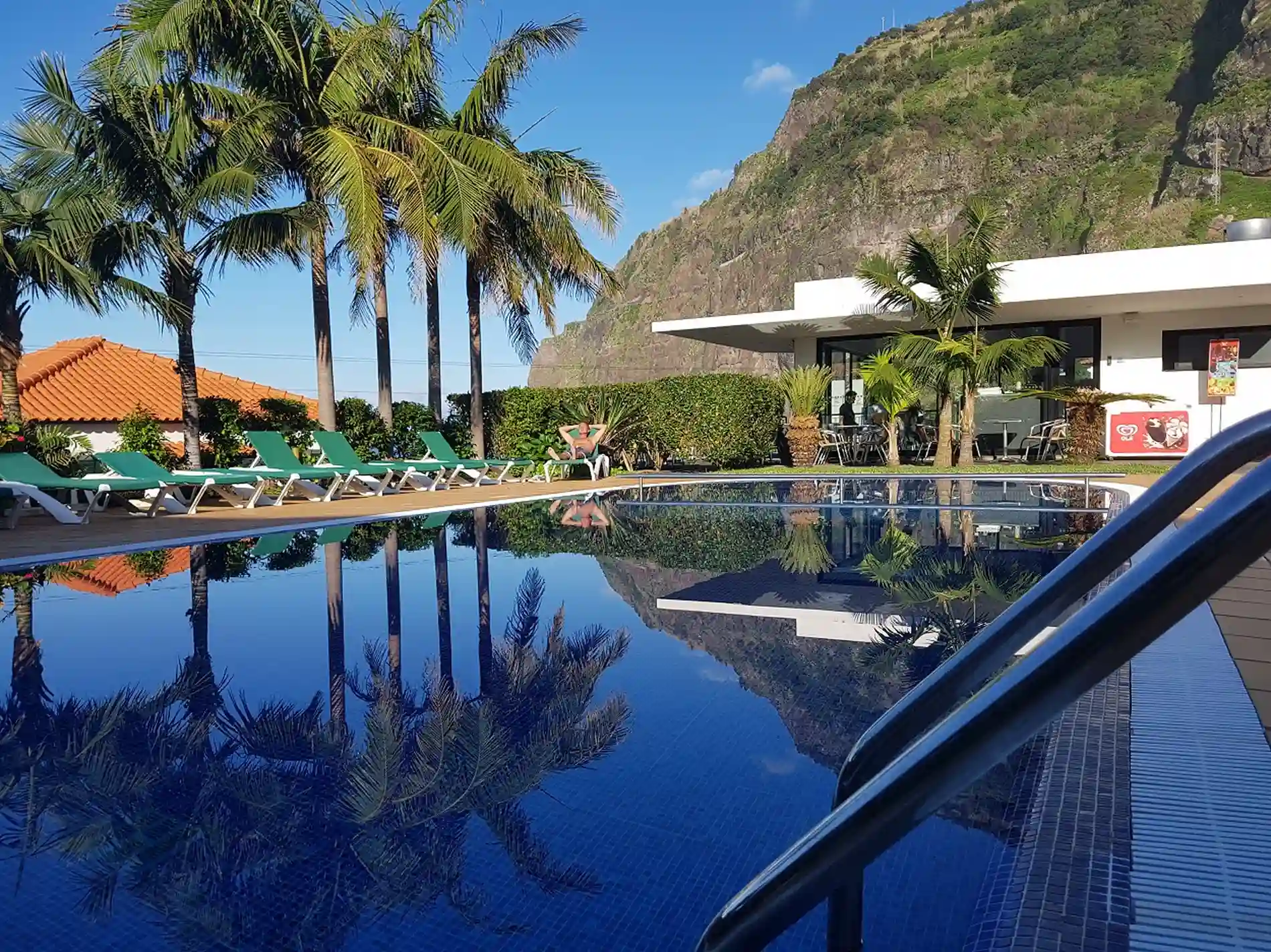 Piscina de hotel com espregui&ccedil;adeiras, palmeiras e vista para montanhas refletidas