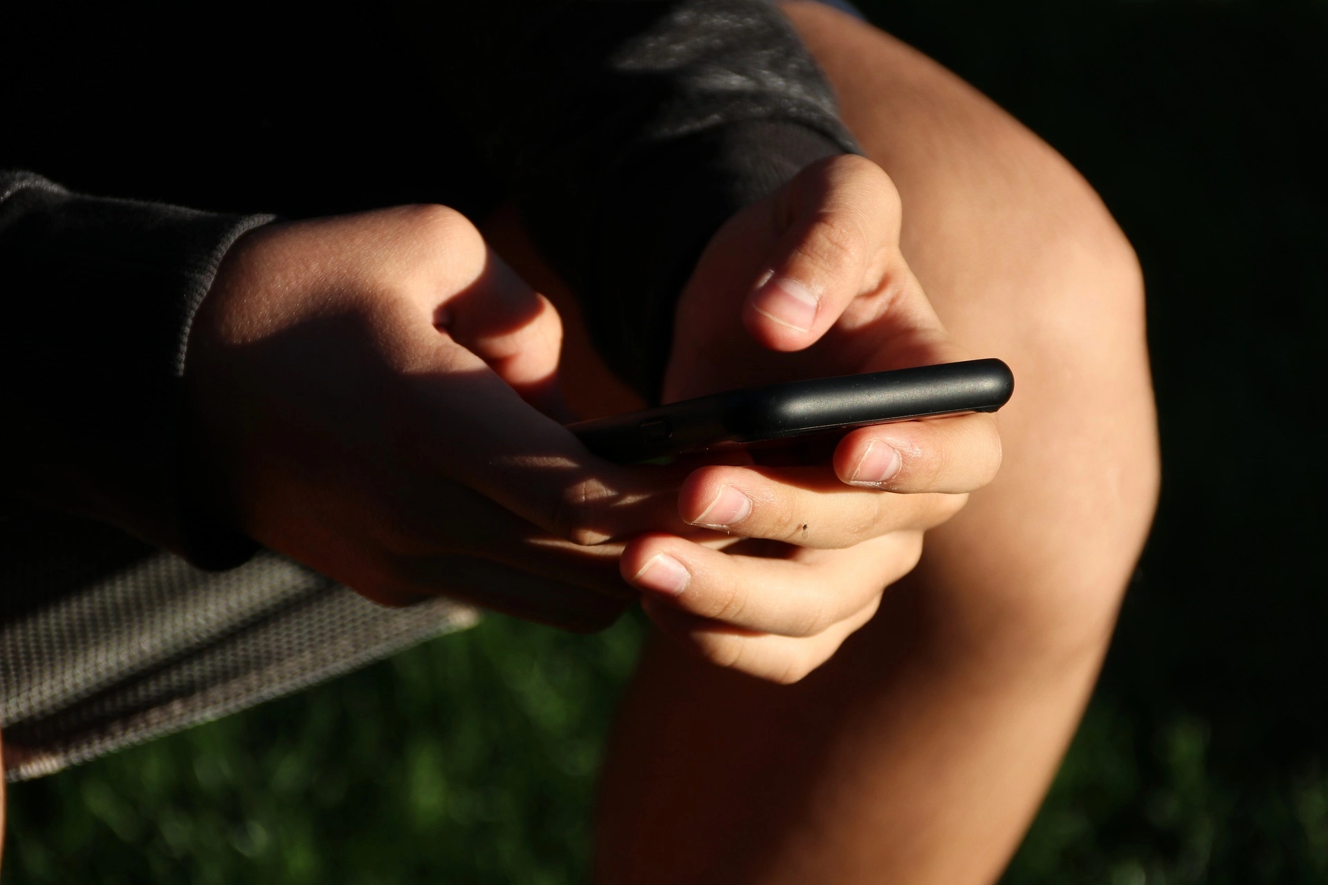 M&atilde;o segura um smartphone na penumbra, com luz lateral destacando os dedos