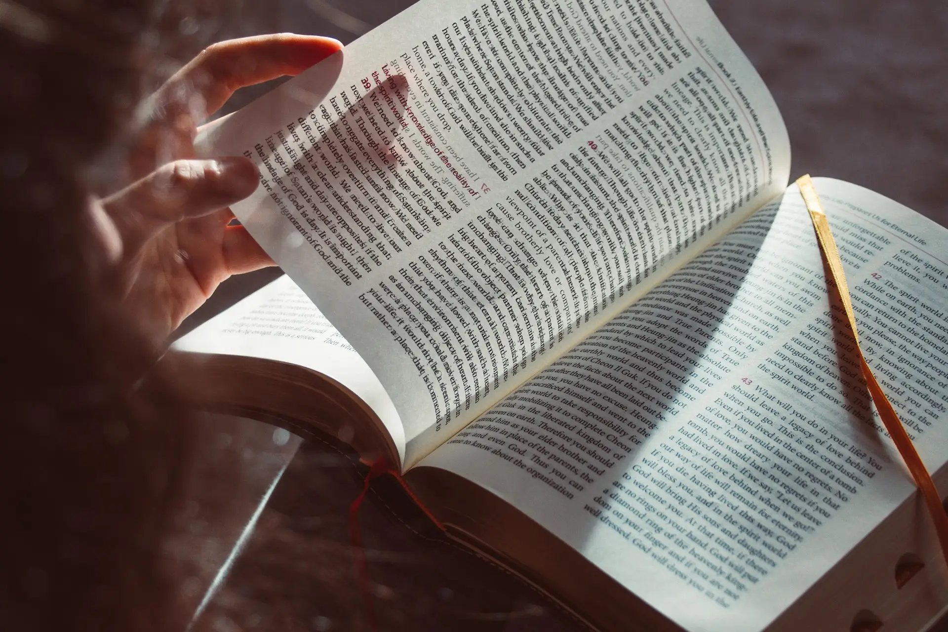 M&atilde;o lendo livro aberto, com p&aacute;gina cheia de texto e marcador vermelho