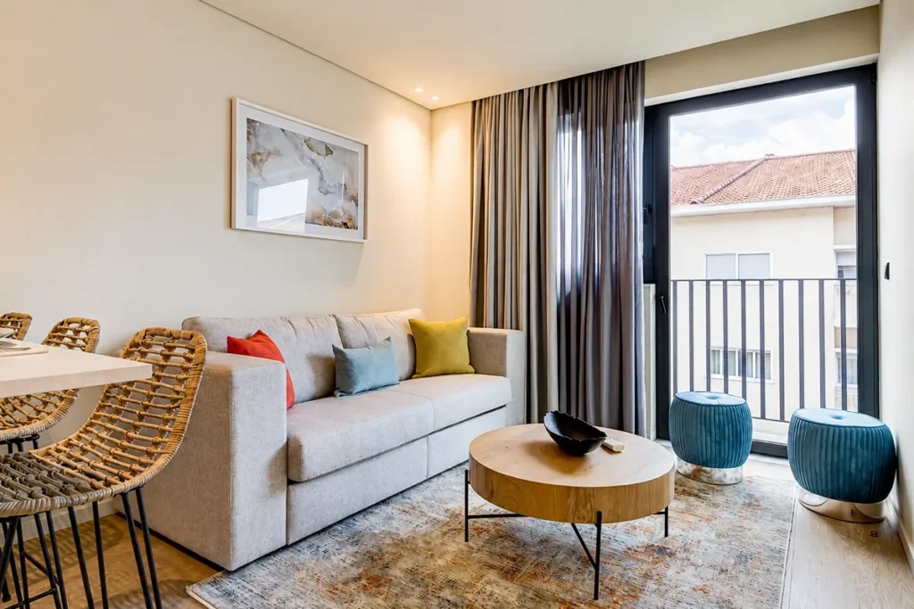 Sala moderna con sof&aacute; gris, mesa redonda y salida a balc&oacute;n con cortinas