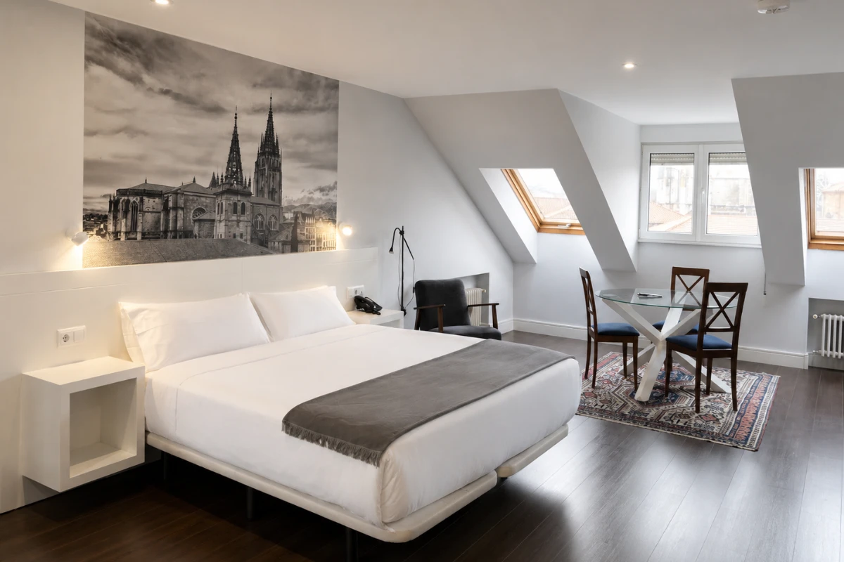 Dormitorio moderno con cama blanca, mesa y silla, y mural de catedral.
