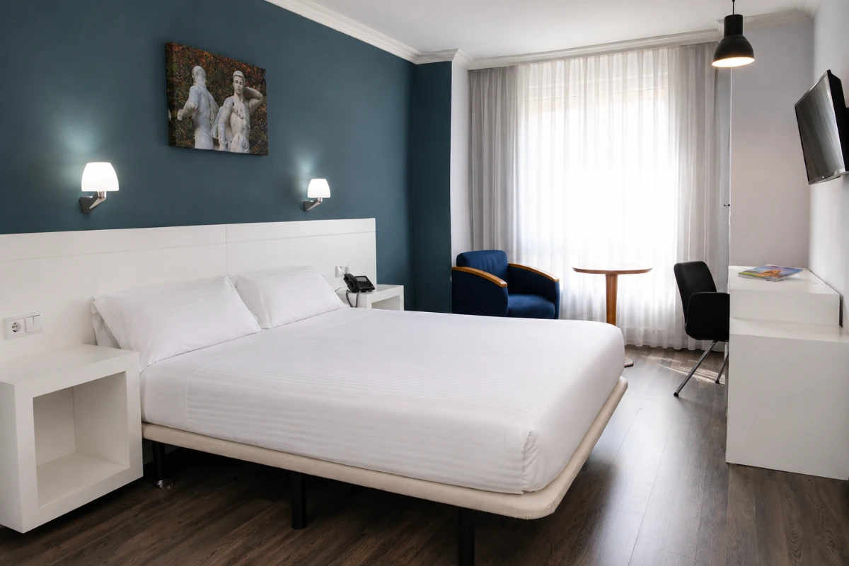 Habitaci&oacute;n de hotel moderna con cama blanca, sillones y cortinas claras