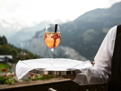 Camarero sirve un c&oacute;ctel rojo en una mesa con monta&ntilde;as al fondo