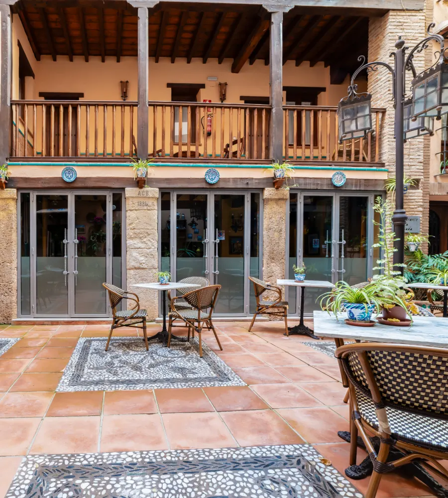 Patio con mesas y sillas de hierro, puertas de vidrio y macetas junto al muro