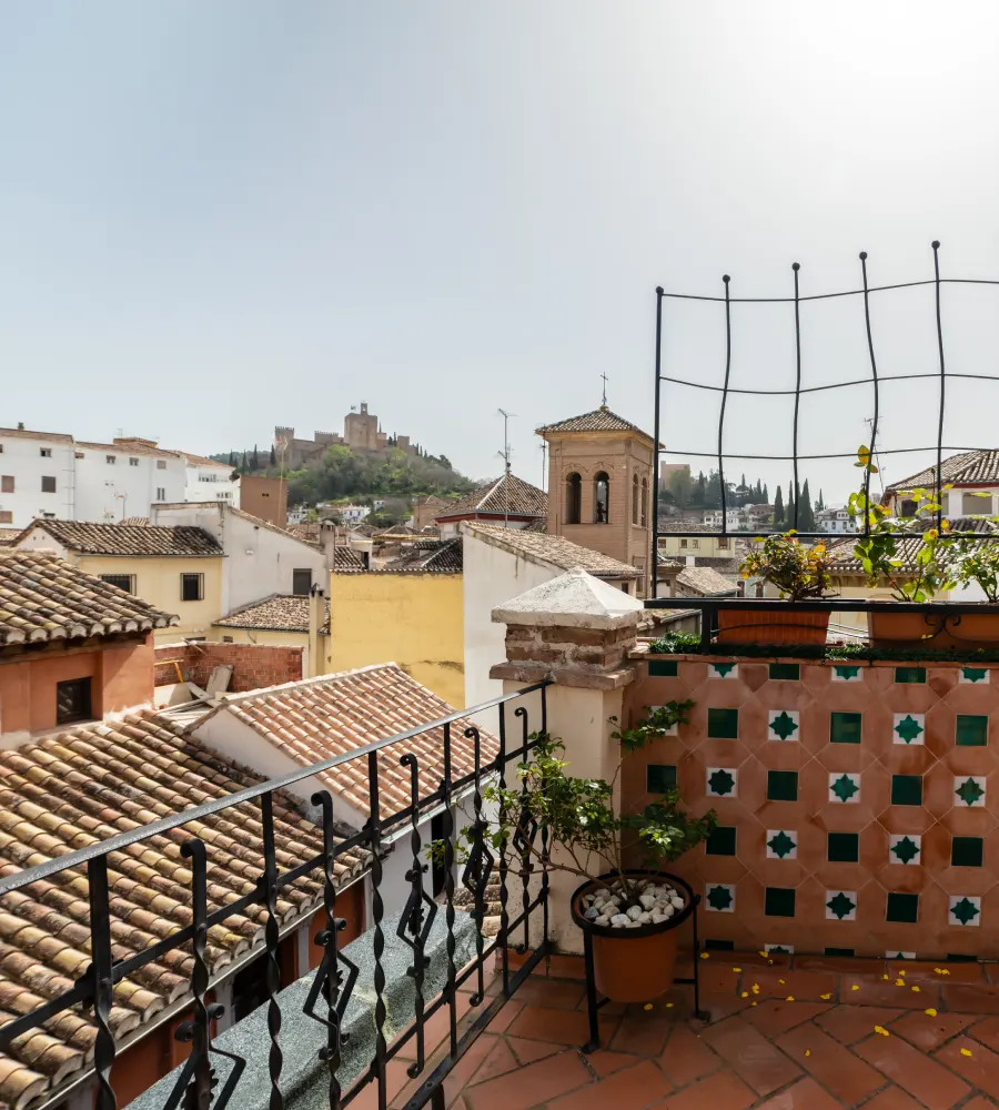Terraza con tejados de teja, reja y iglesia al fondo en el horizonte