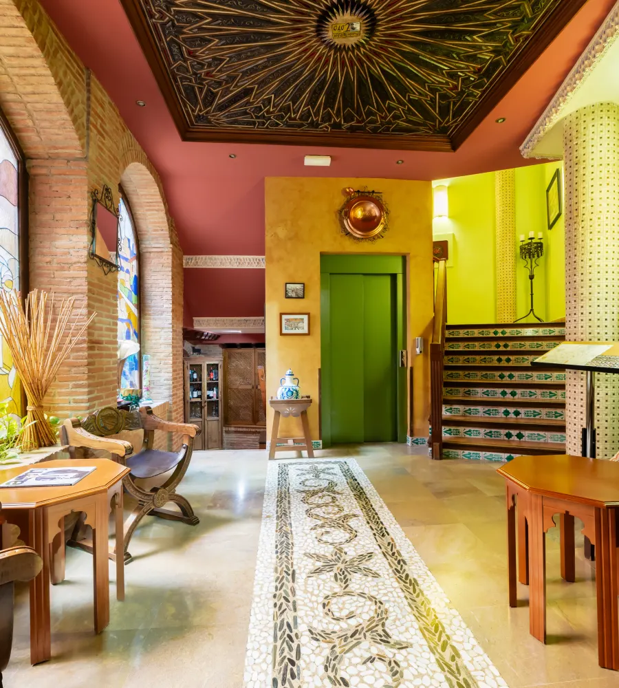 Pasillo interior con techos decorados, mesa y puerta verde, estilo mediterr&aacute;neo