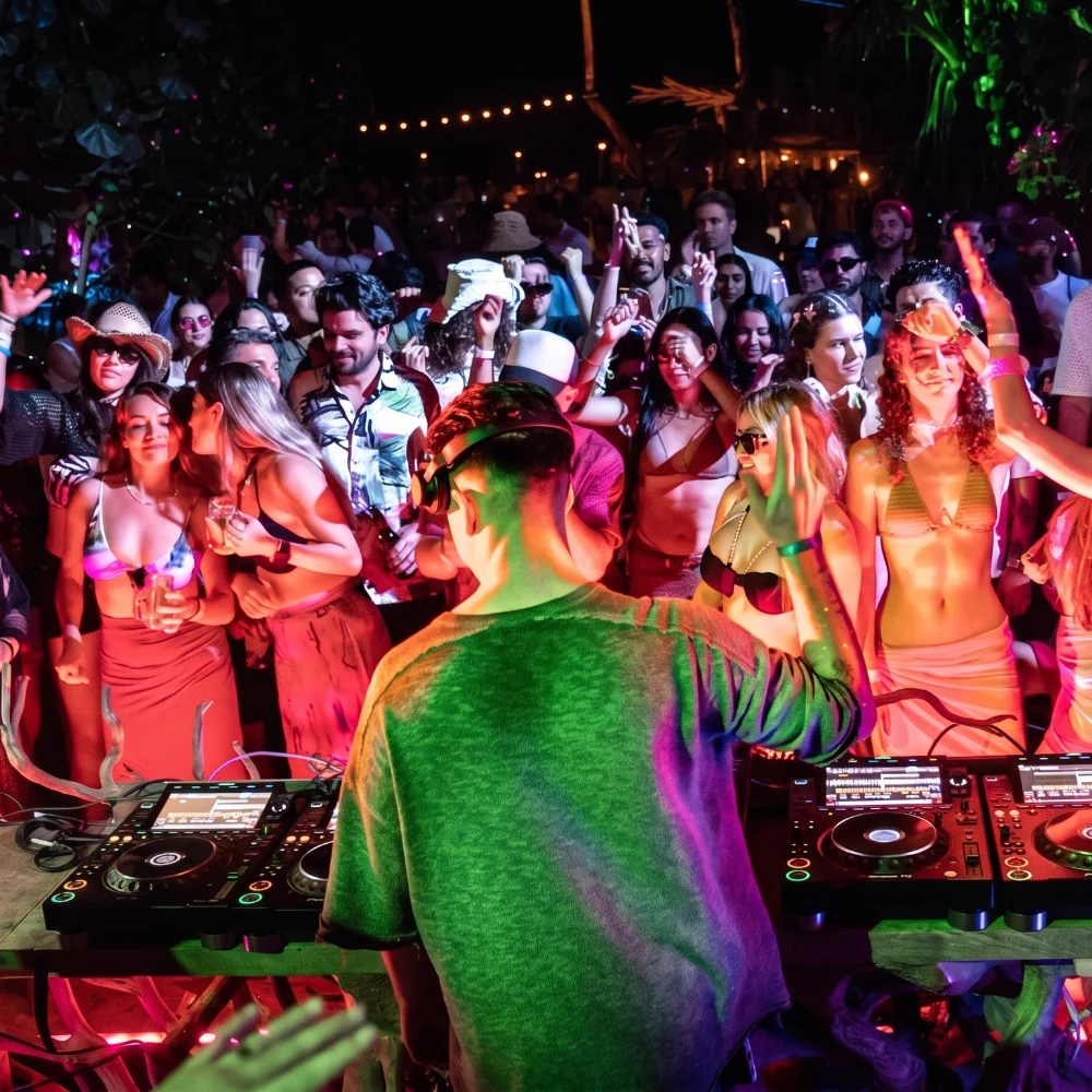 DJ performing behind colorful lights at a crowded club dance party