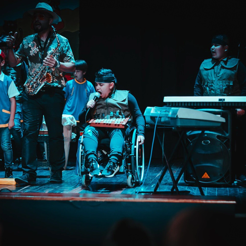 Musician in wheelchair sings with band playing on stage under blue lights