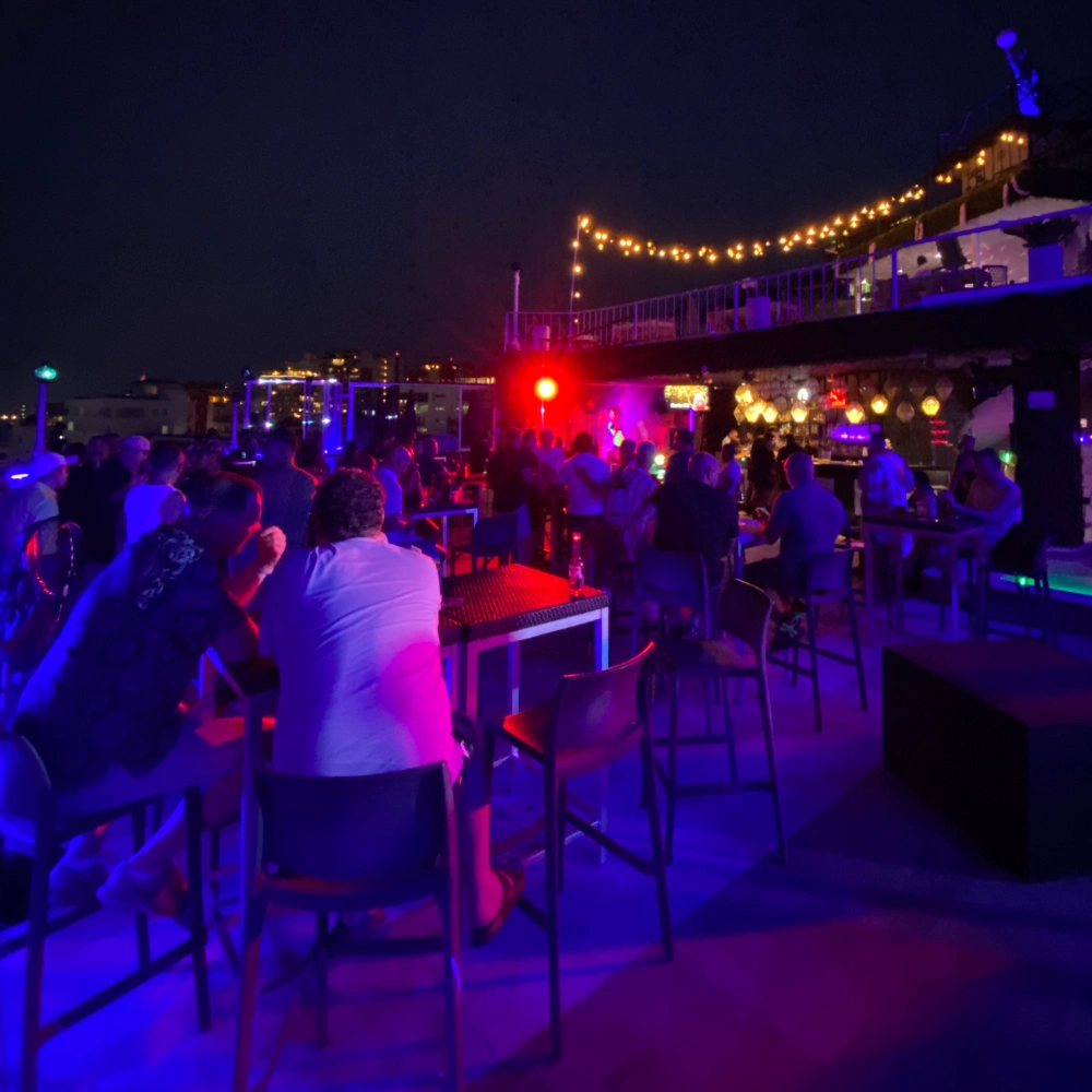 Rooftop party at night with string lights, crowd, and colored stage lighting