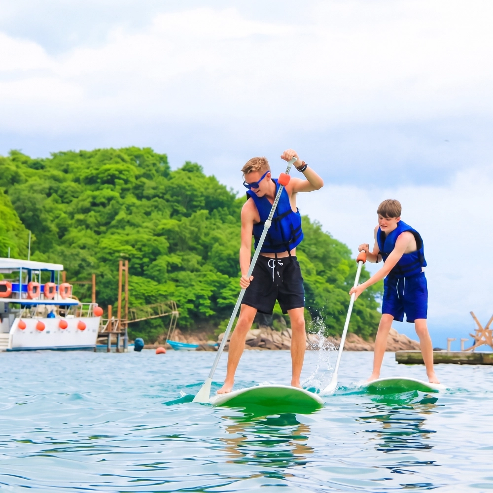Two children in life jackets paddle a green stand-up paddleboard outdoors