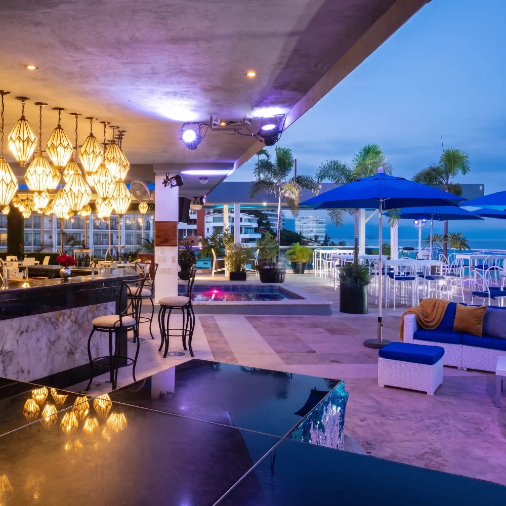 Evening rooftop lounge with pool, string lights, and blue umbrellas