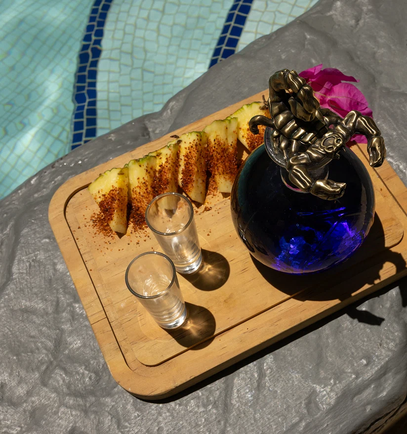 Brass cloche with glowing blue drink and served food on a poolside tray