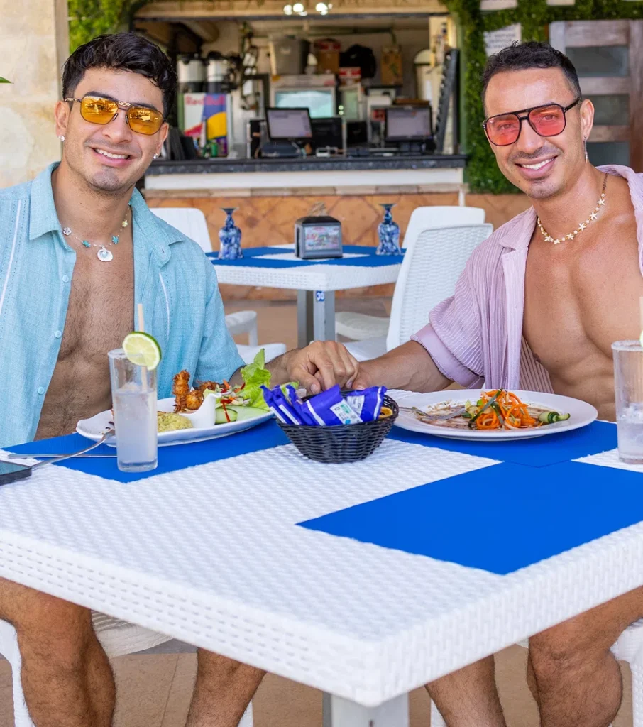 Two men with sunglasses dining at an outdoor restaurant table with food and drinks
