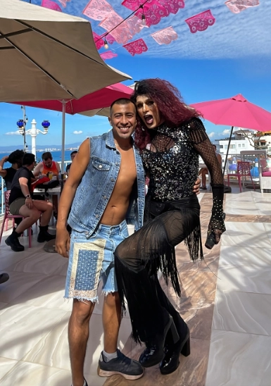 Man in denim with performer in black sequined outfit and red wig at outdoor event