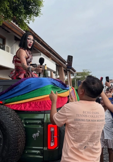 Drag performer holding mic in front of green truck as crowd records on phones