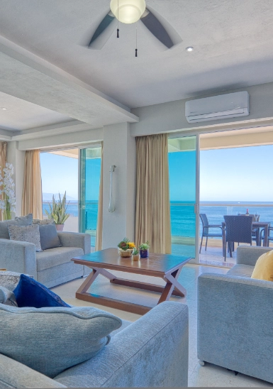 Bright oceanfront living room with blue curtains and seating by large windows