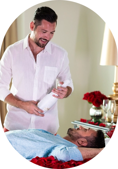 Man smiling as he massages a man lying on a bed with red flowers