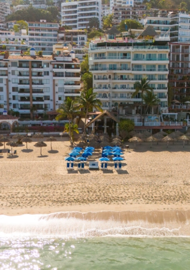 Beachfront resort with ocean waves and rows of blue umbrellas under palm trees