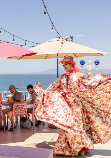Woman in floral dress seated on a deck under a white umbrella by the sea