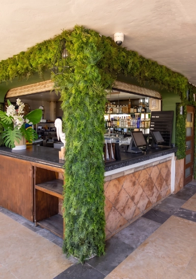 Green moss-covered column in an outdoor bar with shelves and stools