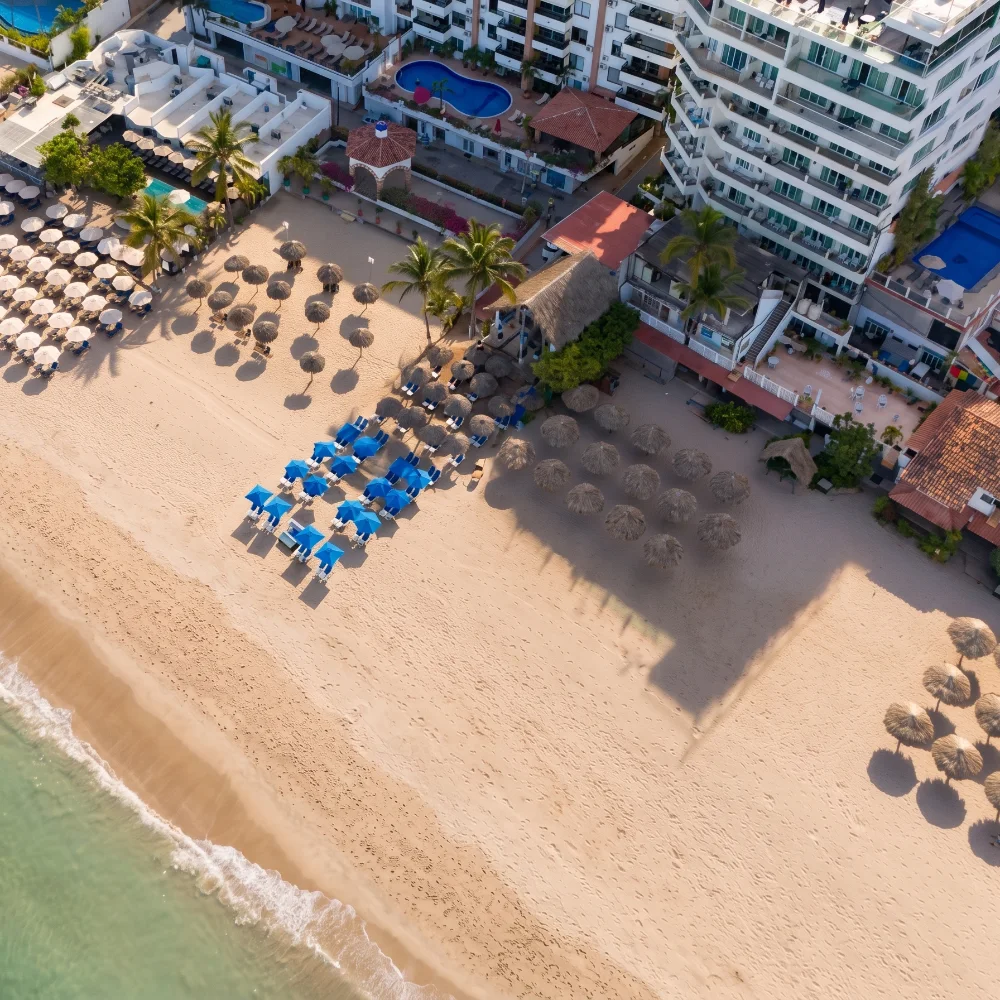 Aerial view of a beachfront resort with blue chairs, pools, and umbrellas
