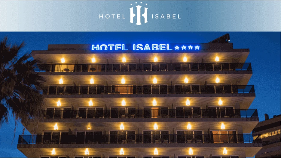 Fachada del Hotel Isabel con luces nocturnas y palmeras frente al edificio