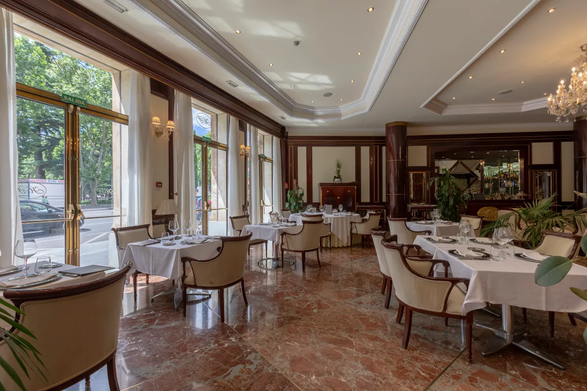 Comedor elegante de hotel con mesas servidas y ventanales con vista a jardín