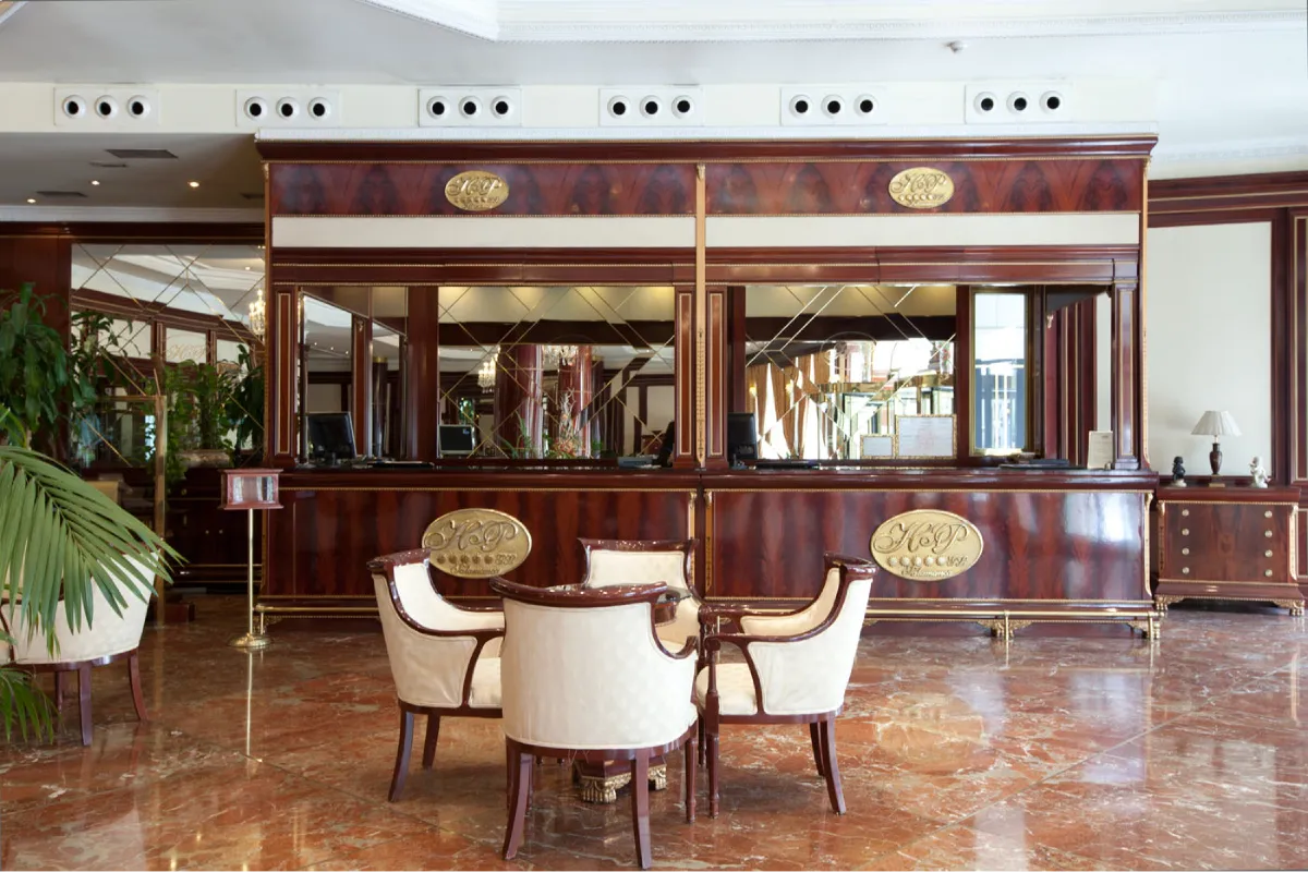 Mostrador de recepción con espejo y asientos en un hotel, estilo clásico.