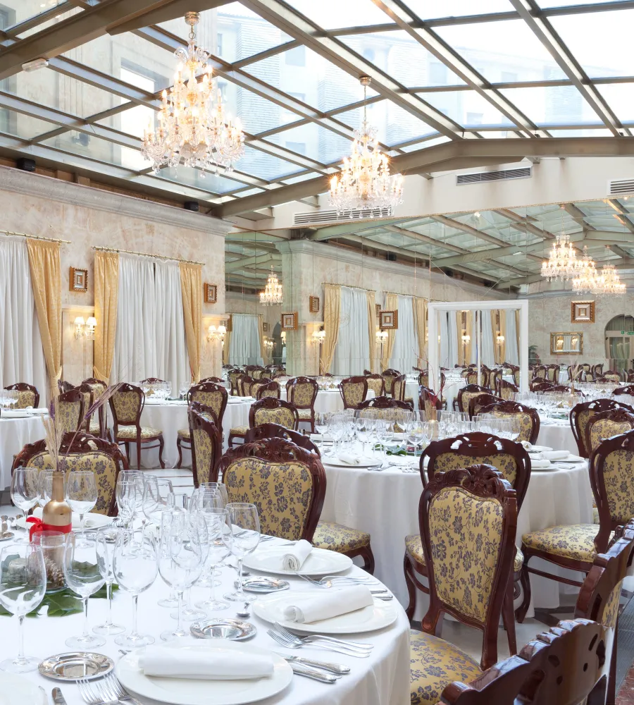 Comedor elegante con mesas servidas, candelabros y techo de cristal.