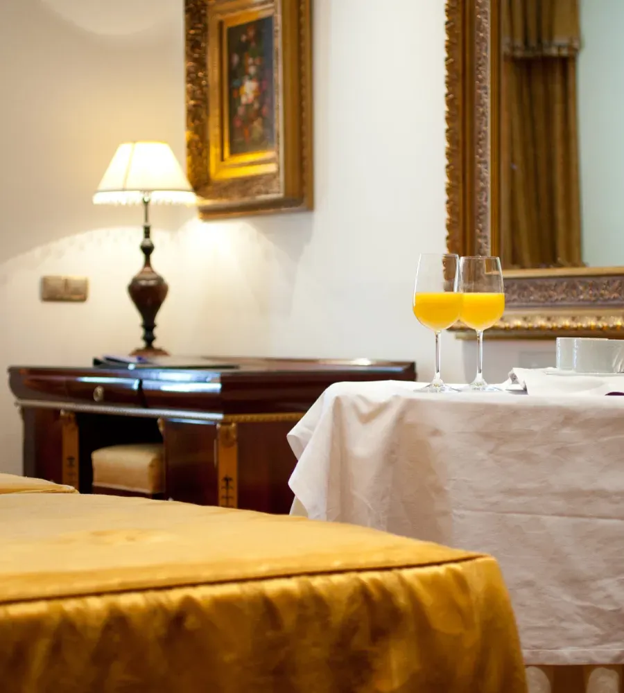 Mesa con dos copas de jugo naranja en un elegante hotel, junto a cama y l&aacute;mpara