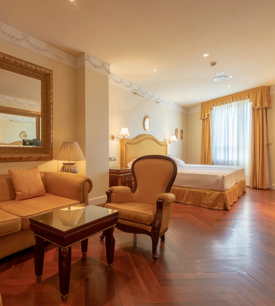 Dormitorio elegante con cama doble, sill&oacute;n y mesa de centro, tonos beige