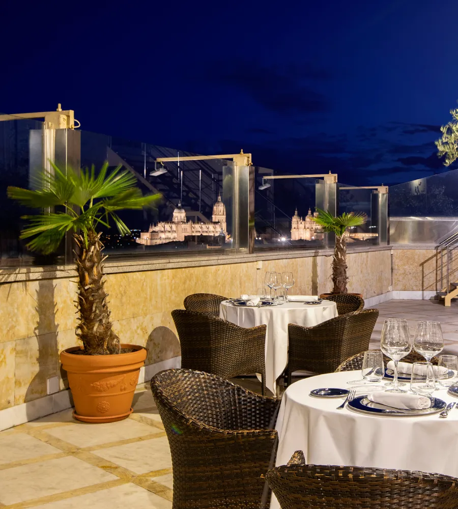 Terraza con mesa puesta y palmeras, vista nocturna del castillo iluminado