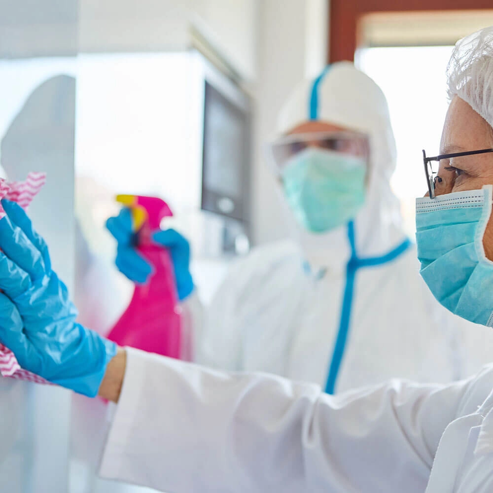 Personal de salud con mascarillas en un entorno cl&iacute;nico, limpiando.