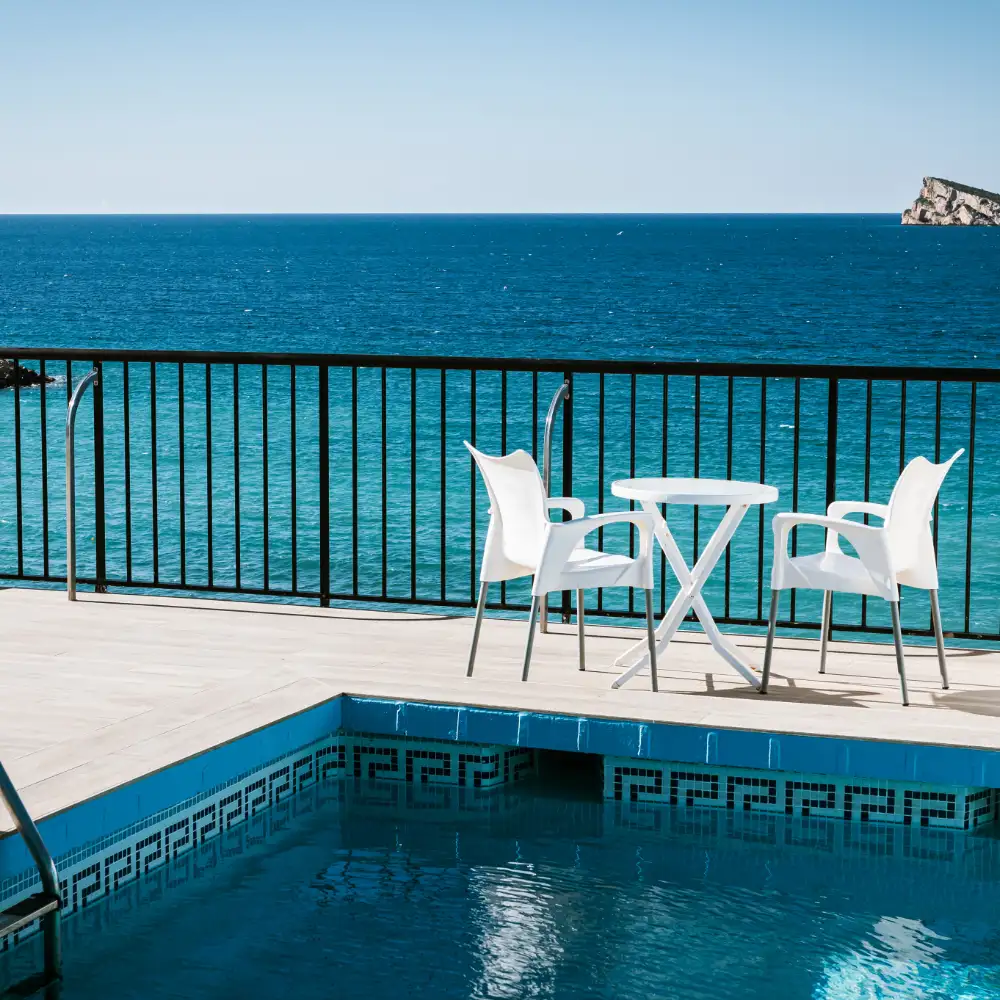 Piscina con sillas blancas y vista al mar azul desde un balc&oacute;n