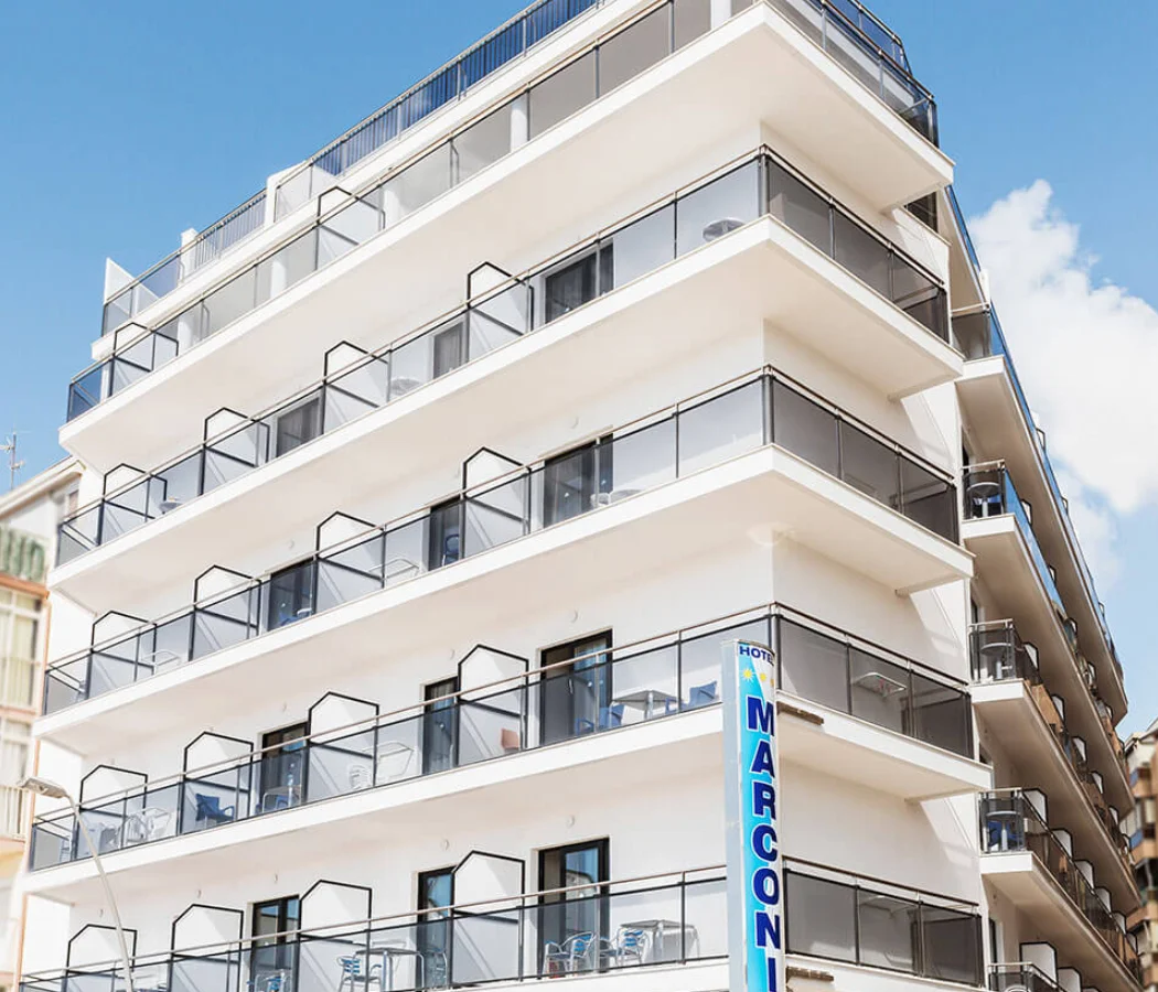 Hotel con balcones y fachada blanca, vista desde la calle bajo cielo azul