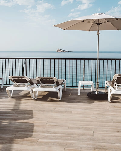 Terraza con tumbonas y sombrilla junto al mar, con vista al horizonte.
