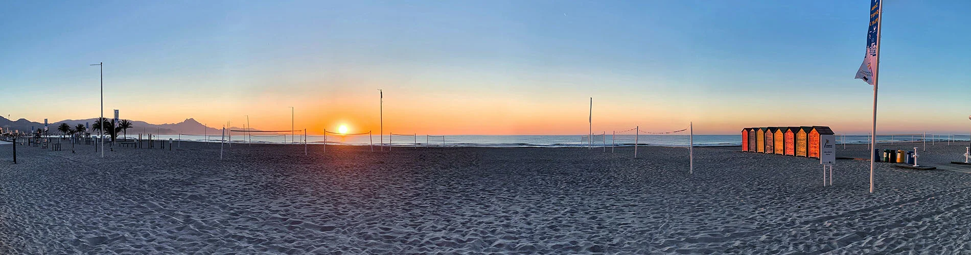 Amanecer en una playa con huellas de arena y postes junto al mar