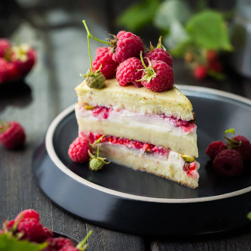 Tarta de queso con frambuesas y crema, decorada con frutos rojos en plato.