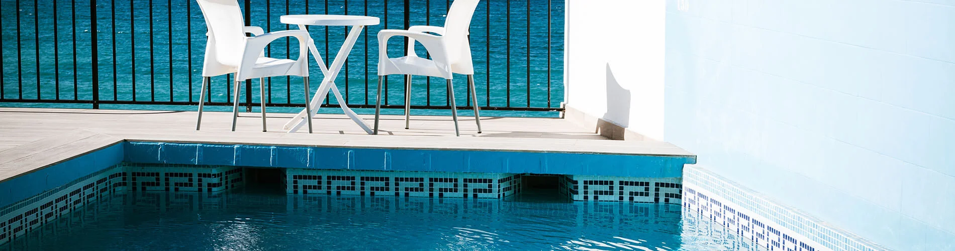 Piscina con sillas blancas junto al mar, vista desde la terraza.